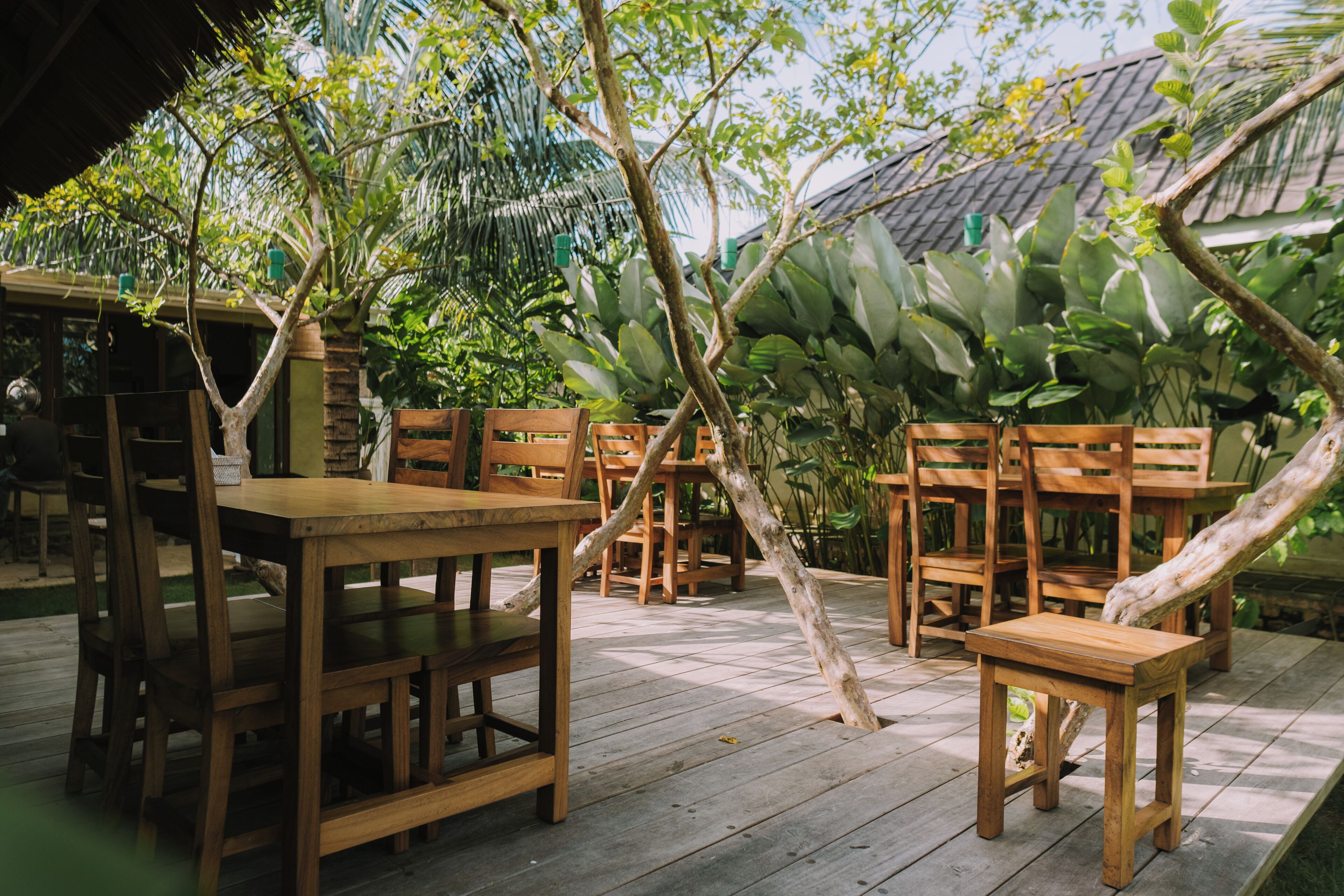 An outdoor wooden deck with tables and chairs, surrounded by lush tropical plants.