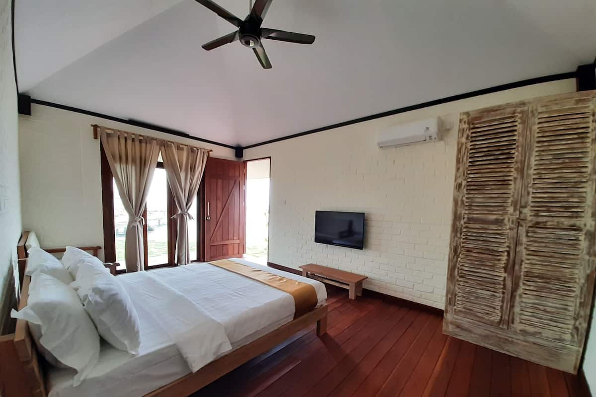 A bedroom with a wooden bed, a ceiling fan, a television, and a window with curtains.