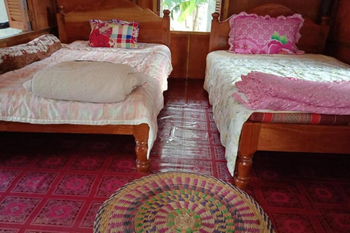 Une pièce avec deux lits en bois, chacun recouvert d’une couvre-lit et agrémenté d’oreillers aux motifs différents. Un tapis tissé est posé sur le sol, devant les lits.