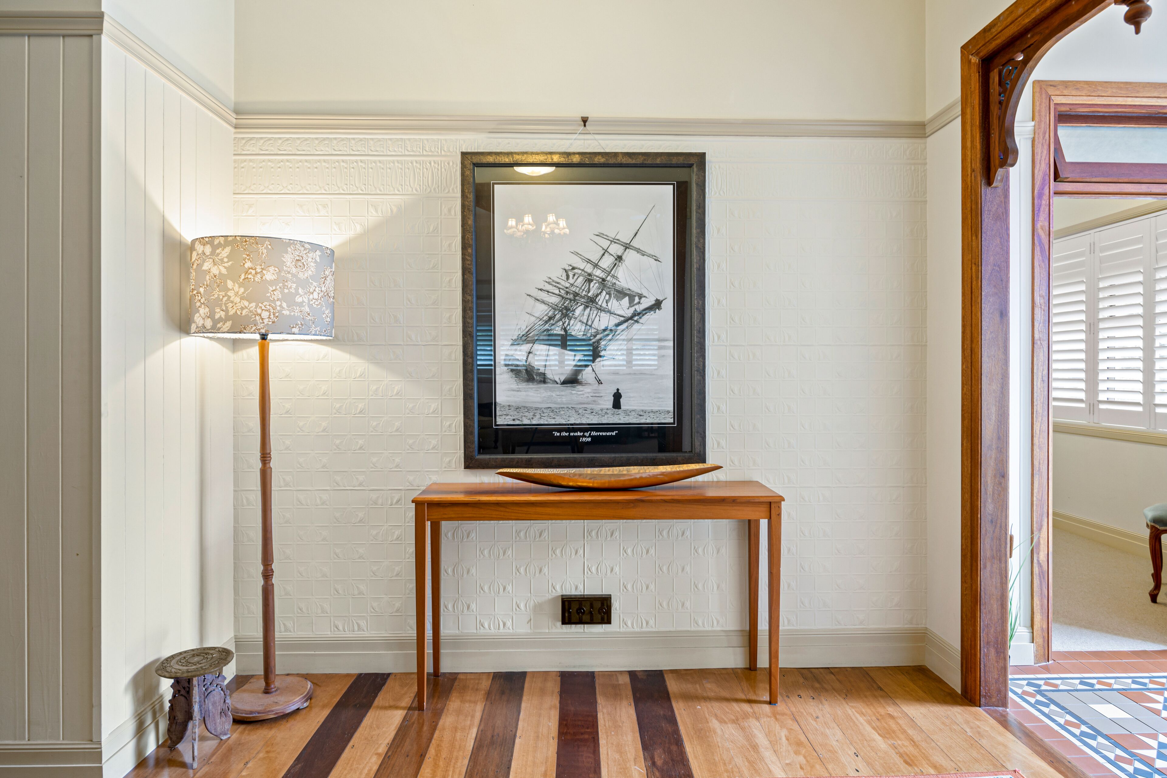 Un couloir avec une console en bois, une œuvre d’art encadrée et un lampadaire.