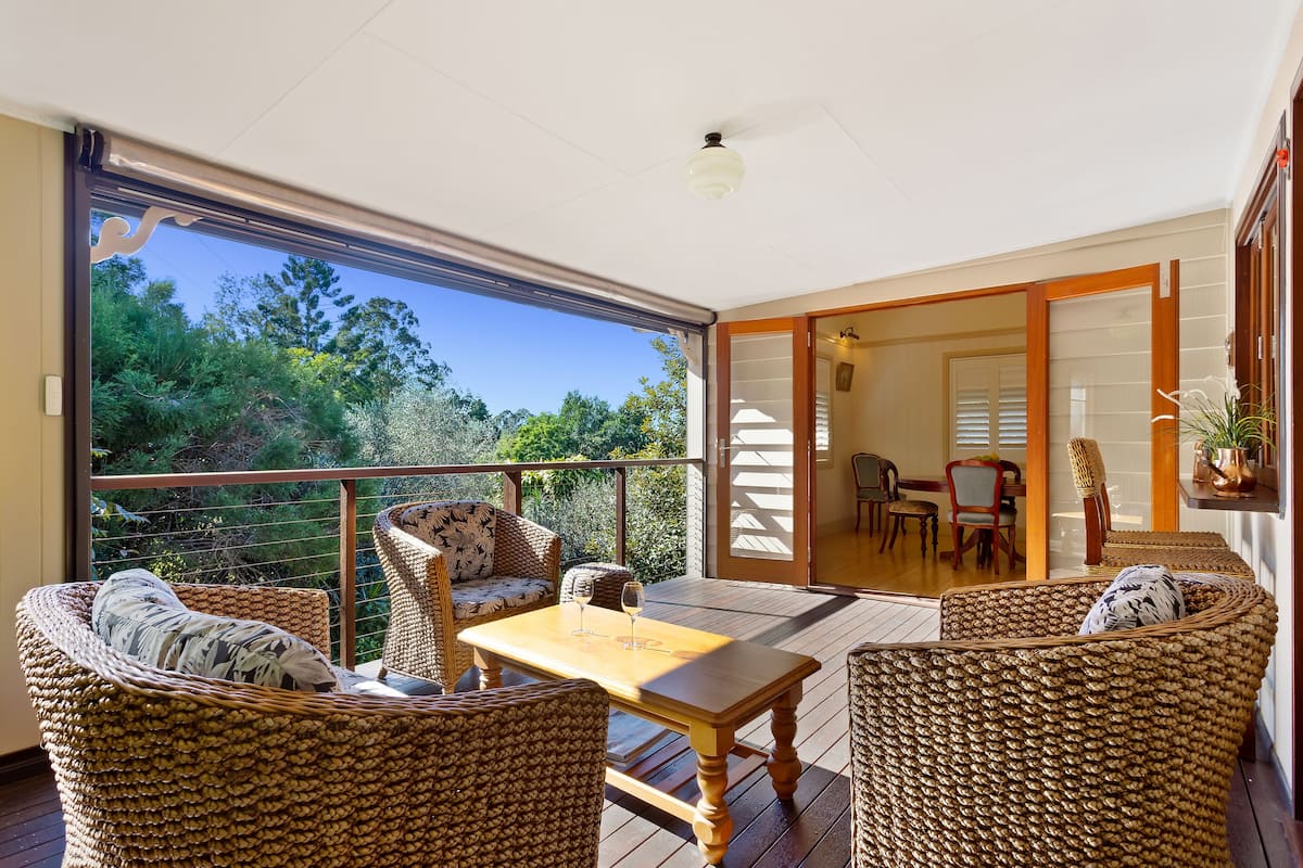 A balcony with wicker furniture, a wooden table, and a view of the outdoors.