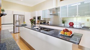 A modern kitchen with a central island, stainless steel appliances, and a large window. - The Guesthouse (Maleny)