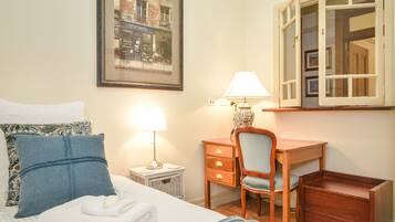A neatly arranged hotel room with a bed, a desk, a chair, a lamp, and a framed picture on the wall.