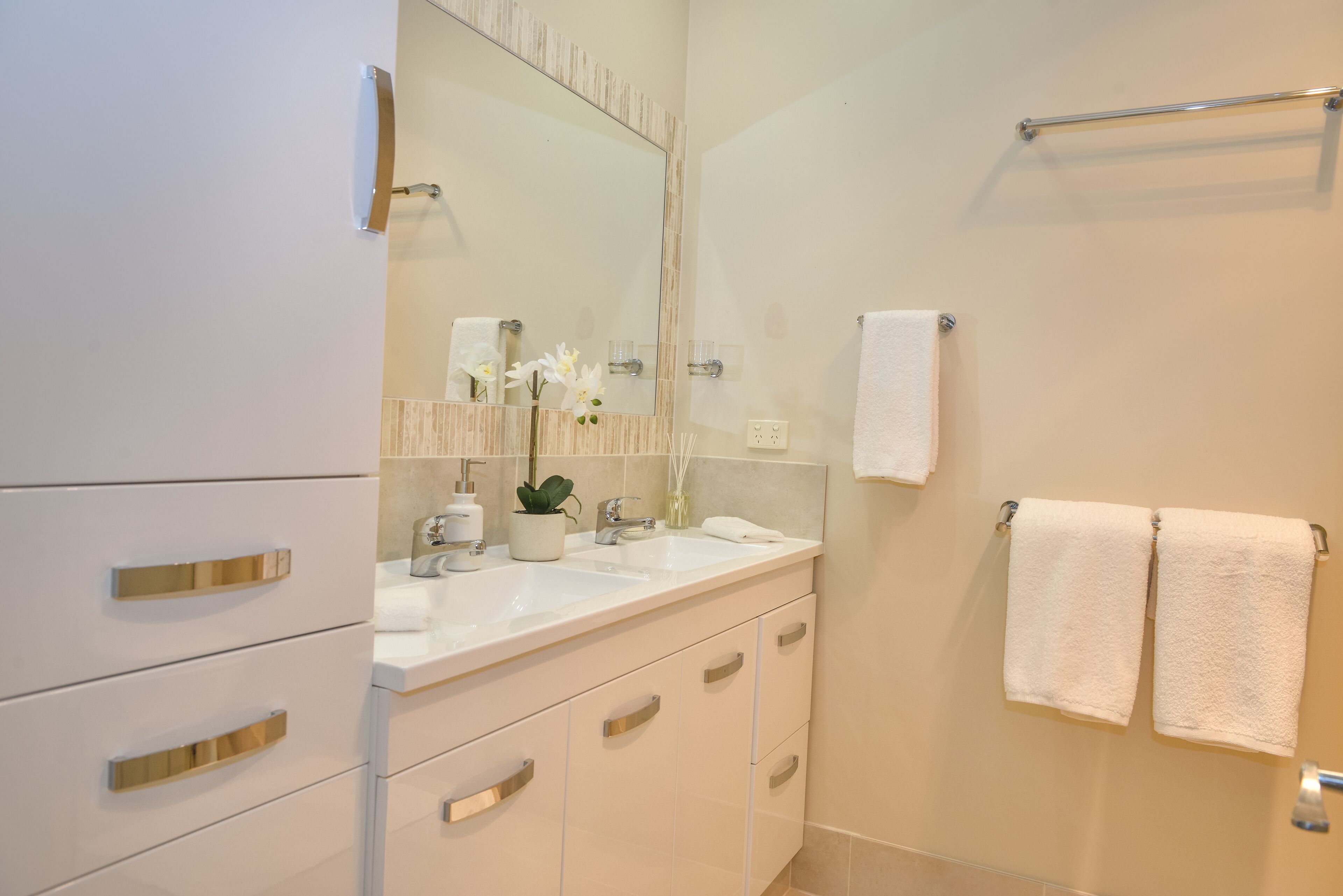 A modern bathroom with a white vanity, a large mirror, and two towels hanging on a rack.