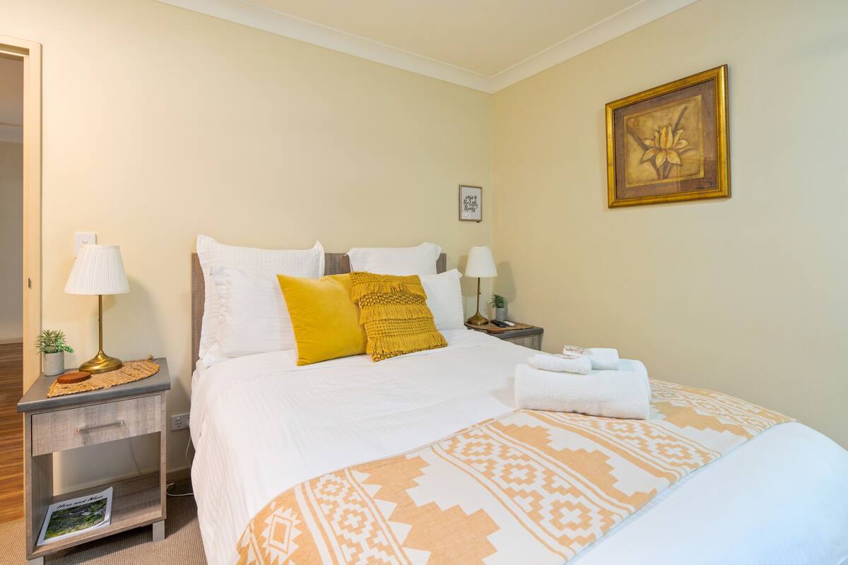 A neatly arranged hotel room with a bed, two bedside tables, a nightstand, a lamp, and a wall-mounted picture.