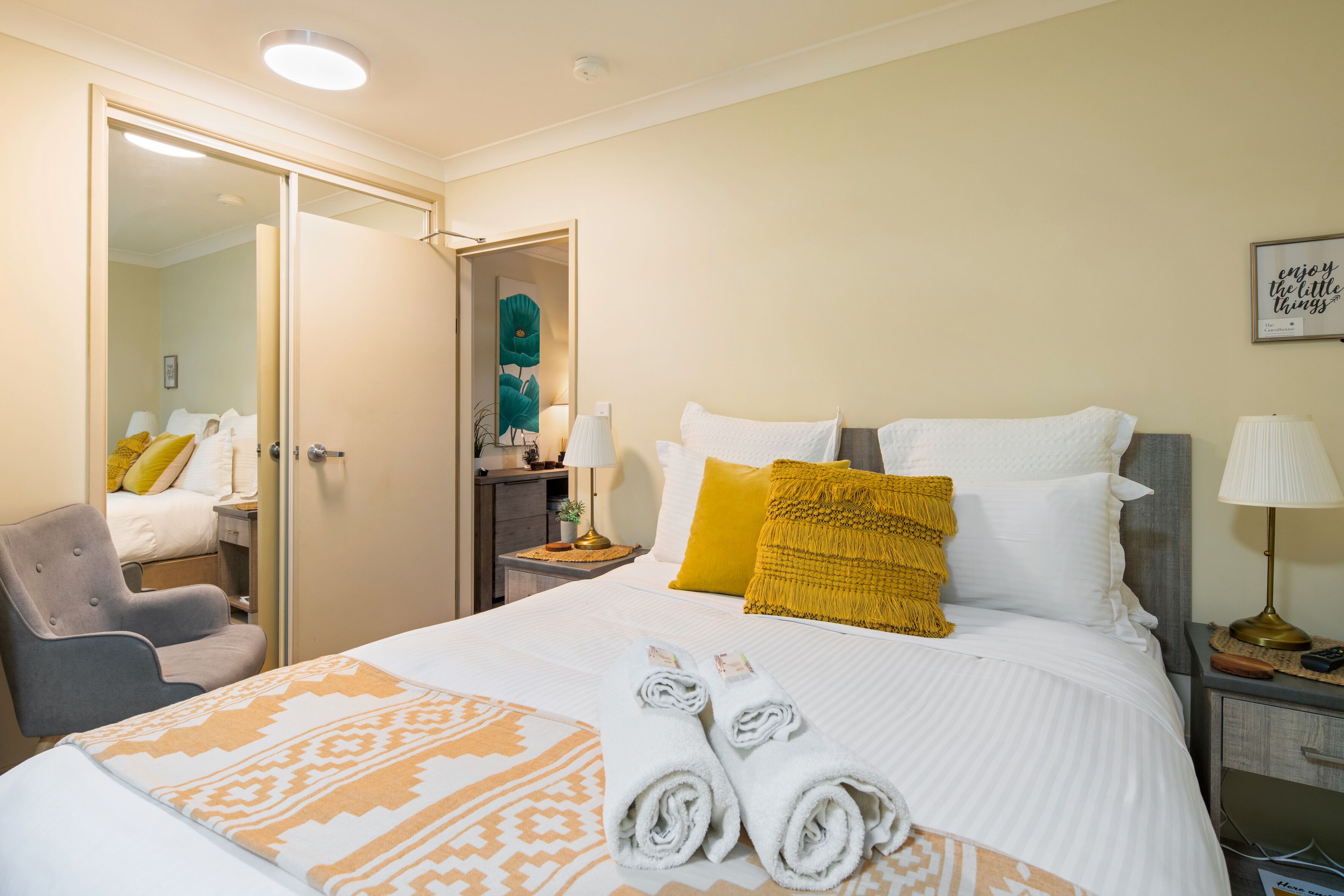 Een hotelkamer met een bed, een stoel, een nachtkastje en een spiegel.
