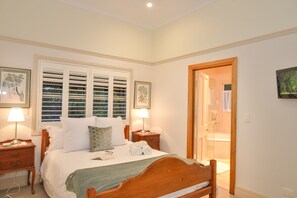 Un dormitorio ordenado con una cama grande, mesitas de noche, una ventana con persianas y una puerta que da al baño.