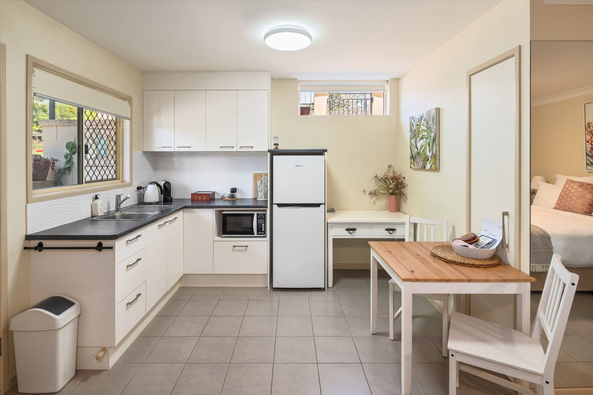 A compact kitchen with a refrigerator, microwave, and kettle. There is a small dining area with a table and chairs.