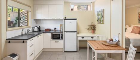 A compact kitchen with a refrigerator, microwave, and kettle. There is a small dining area with a table and chairs.