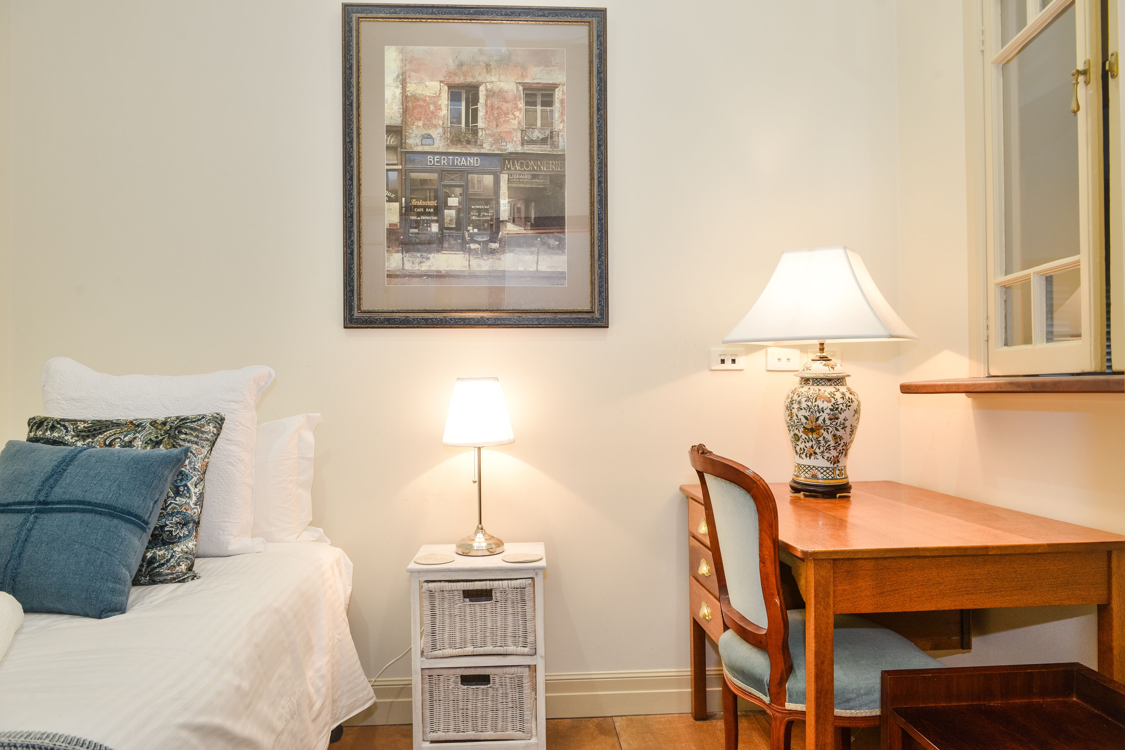 Une chambre bien rangée, avec un lit, une table de chevet sur laquelle se trouve une lampe, une chaise et un tableau encadré accroché au mur.