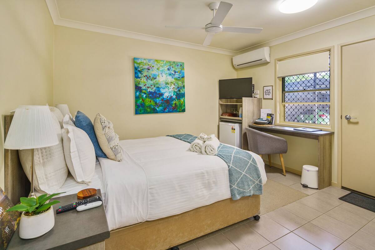 A bedroom with a bed, desk, and chair, a ceiling fan, and a window with a view.