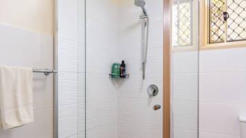A glass-enclosed shower with a handheld showerhead, a toilet, and a trash bin.