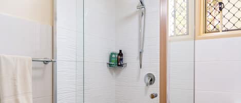 A glass-enclosed shower with a handheld showerhead, a toilet, and a trash bin.