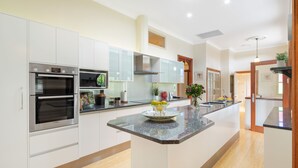 A modern kitchen with built-in appliances, a central island, and a view to the dining area. - The Guesthouse (Maleny)