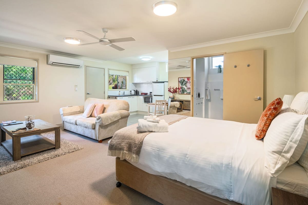 A hotel room with two beds, a sofa, a small table, a kitchenette, and a bathroom with a shower.