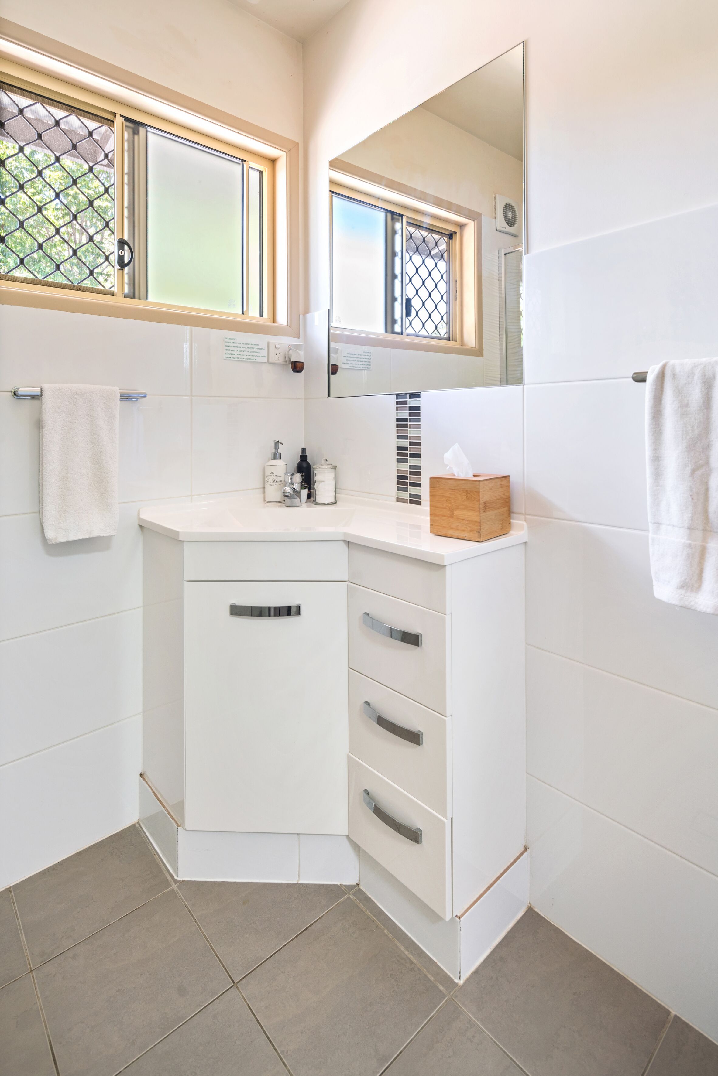 A modern bathroom with white cabinetry, a mirror, and a window with a decorative grid pattern.