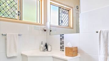 A modern bathroom with white cabinetry, a mirror, and a window with a decorative grid pattern.