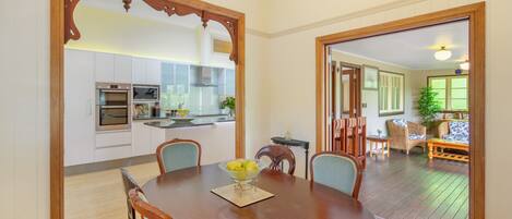 Un comedor con mesa y sillas de madera, una cocina al fondo y vistas a un patio con mobiliario exterior.