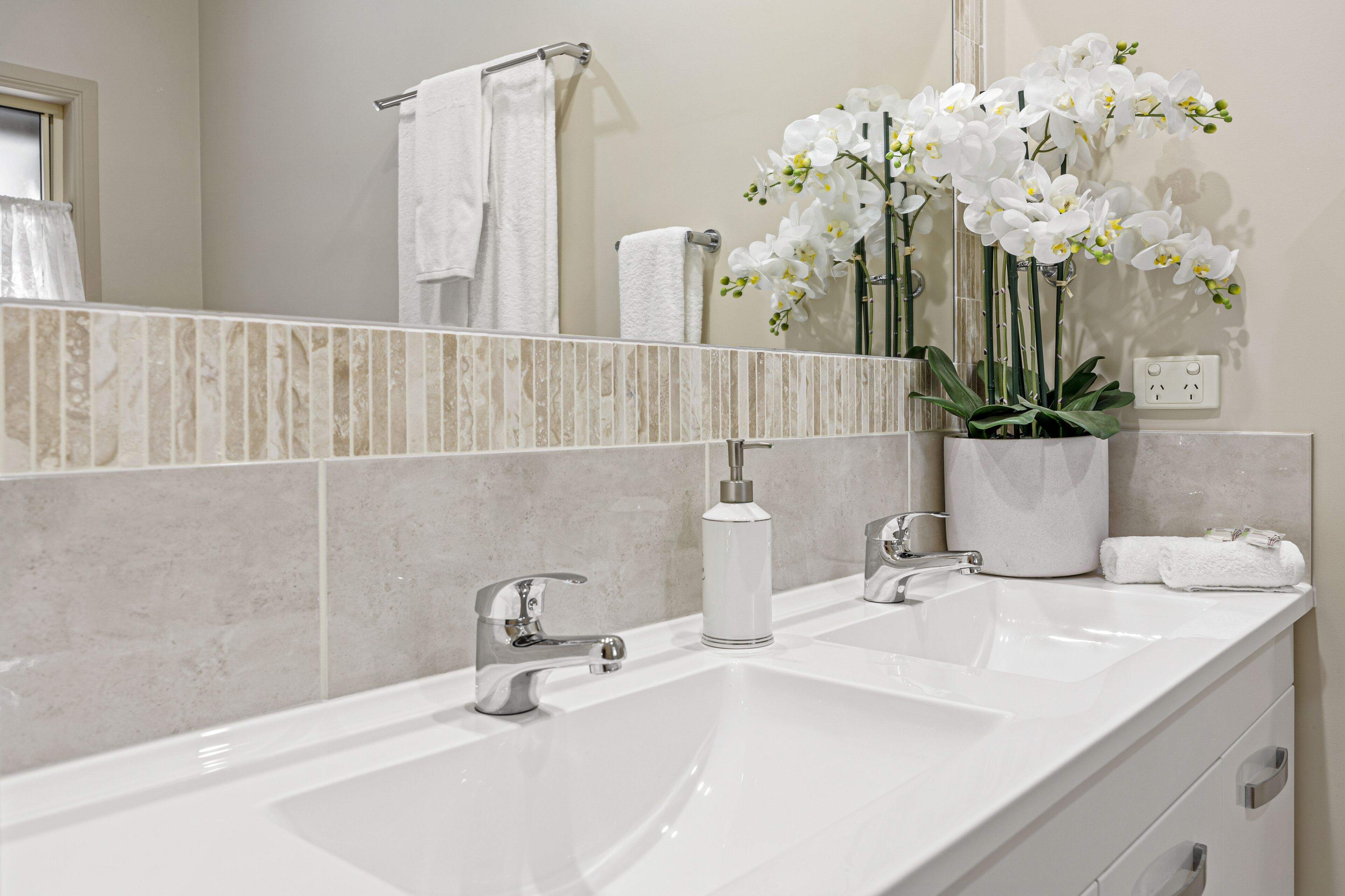 Un baño con un lavabo blanco, un espejo y una orquídea en maceta.