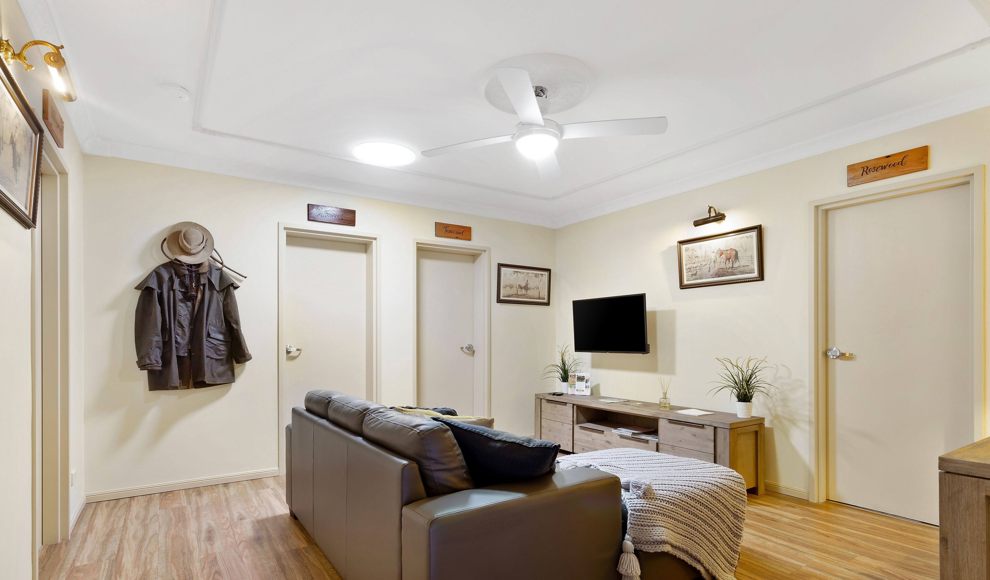 Una stanza con ventilatore a soffitto, un letto, una scrivania, una TV e un appendiabiti.