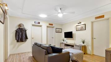A room with a ceiling fan, a bed, a desk, a TV, and a coat rack.