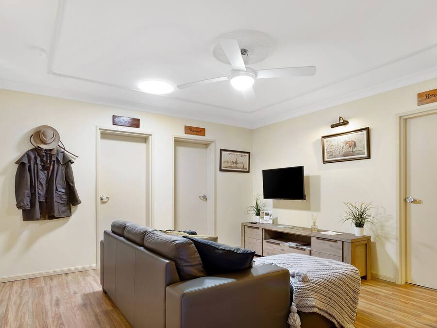 A room with a ceiling fan, a bed, a desk, a TV, and a coat rack.