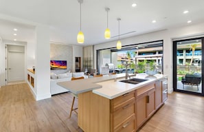 A modern kitchen with a central island, pendant lighting, and a view of a pool and buildings.