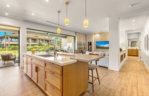 A modern kitchen with wooden cabinets, a central island, pendant lighting, and a view of the outdoor area.