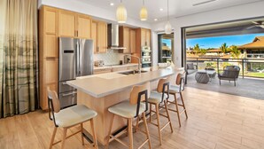 A modern kitchen with wooden cabinets, a stainless steel refrigerator, and a large island with bar stools.