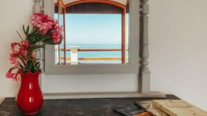 A room with a view of the sea through a window, a red vase with flowers, and a table with books. - Santa Maria by Interhome (Marina di Caronia)