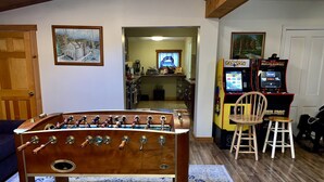 A cozy living room with a foosball table, a kitchen in the background, and arcade games. - Hunter Mountain Getaway House, newly renovated (Hunter)