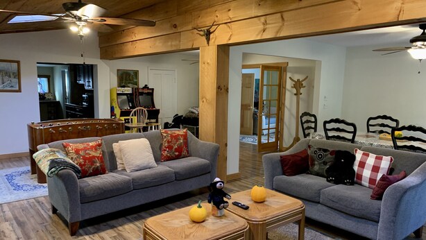A cozy living room with two sofas, a coffee table, and a ceiling fan. There is a wooden dining table and chairs in the background, and a hallway leading to another room. - Hunter Mountain Getaway House, newly renovated (Hunter)