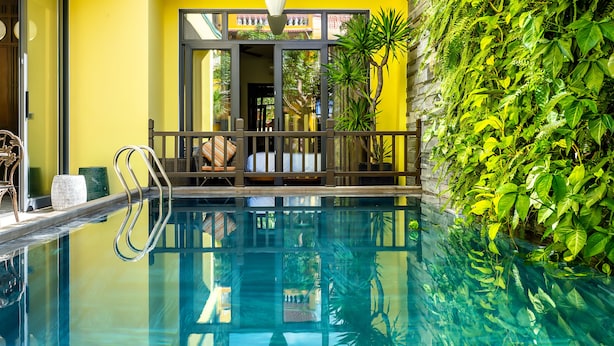 A swimming pool with clear water, surrounded by a yellow wall and a lush green plant wall. - Villa Soleil Hoi An (Da Nang)