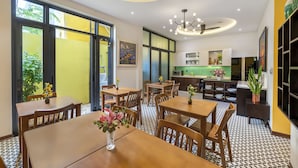 A modern dining area with wooden tables and chairs, a central chandelier, and a view of the kitchen in the background. - Villa Soleil Hoi An (Da Nang)