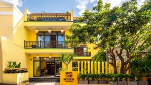 A yellow villa with a balcony, a sign reading "SOLEIL VILLA NOI AN," and a well-maintained garden. - Villa Soleil Hoi An (Da Nang)
