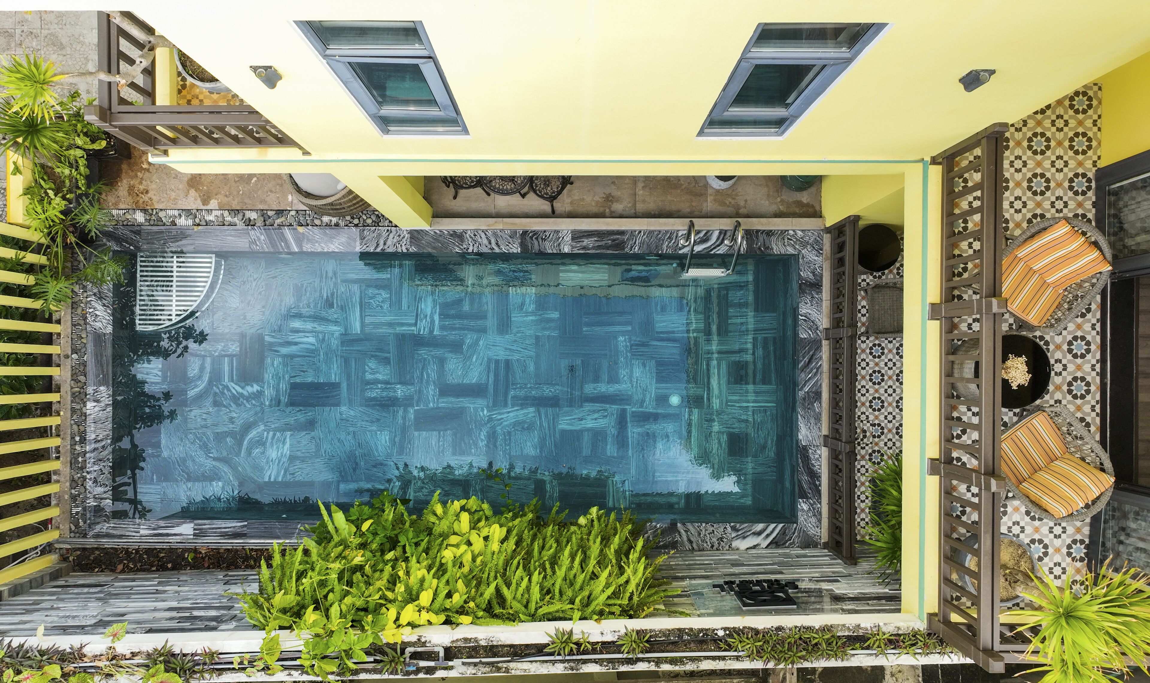 Una piscina con fondo de cristal, rodeada de plantas y un muro decorado.