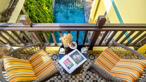 A balcony with wicker furniture, a small table with a vase and a photo, and a view of a swimming pool. - Villa Soleil Hoi An (Da Nang)