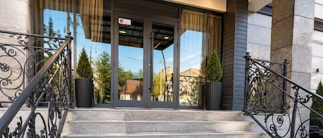 A set of stone steps leading to a building entrance with a glass door, metal railings, and a clear view of the sky.
