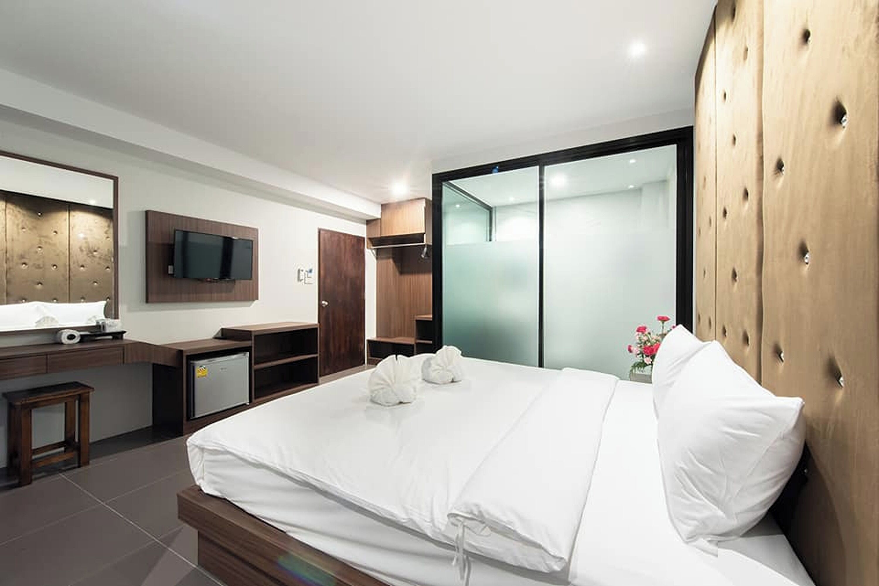 A modern hotel room with a large bed, a television mounted on the wall, a desk with a computer, and a wardrobe with sliding doors.