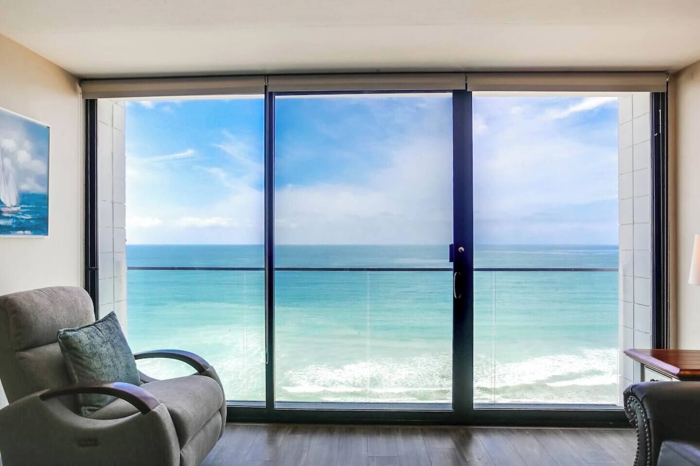 A room with a large sliding glass door leading to a balcony with a view of the ocean.