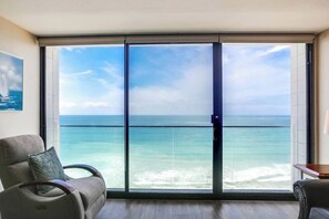 A room with a large sliding glass door leading to a balcony with a view of the ocean.