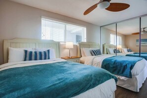Une chambre d’hôtel avec deux lits, un ventilateur de plafond, une table de chevet avec une lampe et un grand miroir.