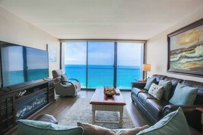 Una sala de estar con una televisión grande, un sofá, una mesa de centro y vistas al océano a través de amplios ventanales.