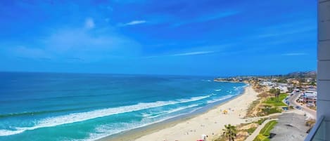 A coastal view with a beach, ocean, and buildings along the shore.