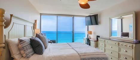 Un dormitorio con una cama grande, ventilador de techo, televisor y vistas al océano.