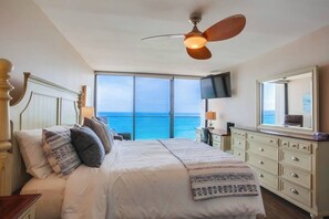 Un dormitorio con una cama grande, ventilador de techo, televisor y vistas al océano.