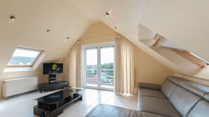 Un appartement moderne de style « loft » doté d’un grand espace de vie, d’un téléviseur, d’une table basse en verre et d’une porte-fenêtre coulissante donnant sur un balcon.