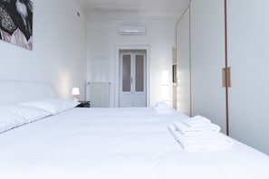 A hotel room with a bed, a nightstand, a radiator, a door, and a wall-mounted air conditioner.