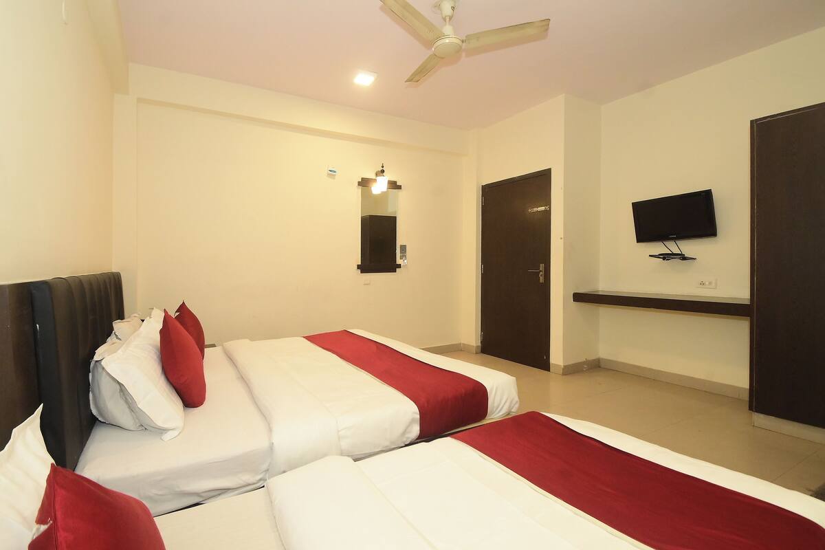 A hotel room with two beds, a ceiling fan, a TV mounted on the wall, and a door.