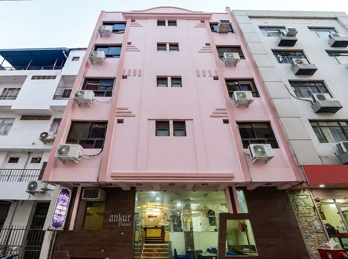 A pink building with multiple air conditioning units, a sign for 'Ankur Palace', and a staircase leading to an entrance.